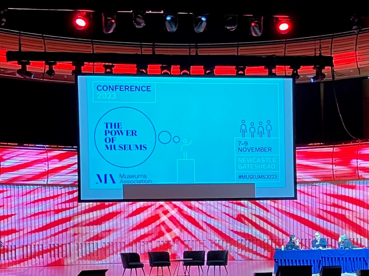 The image shows the conference stage with a screen showing 'The Power of Museums and the Museum Association logo