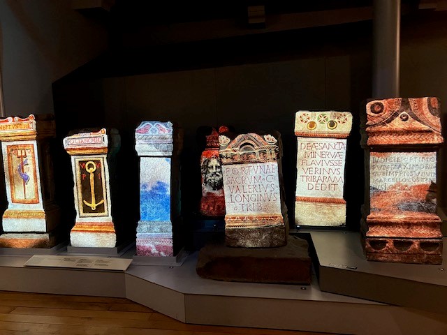 The image shows Roman altars on display with colourful projections on them to highlight the writing and the images