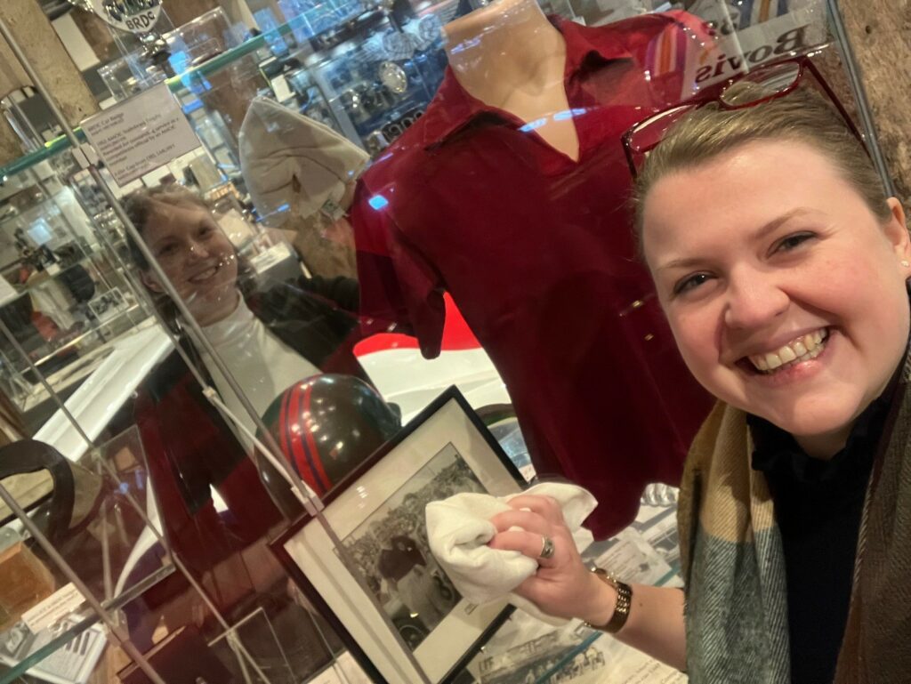 The image shows two women members of AMHT staff cleaning a display case with microfibre cloths