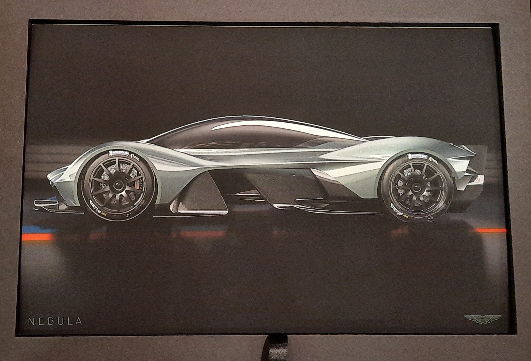 A card from the Nebula Collaboration Presentation Box showing a drawing of the side view of the car. It is a grey colour against a black background with highlights of orange and blue beneath the car