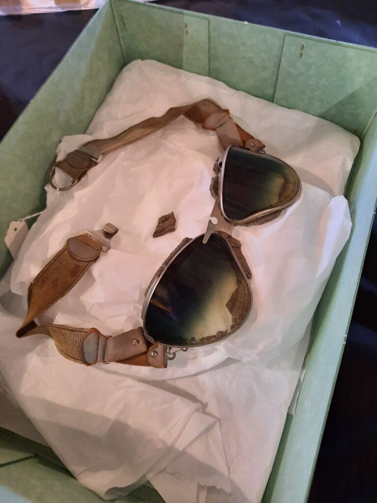 Fragile racing goggles on a bed of tissue paper within a green acid free box