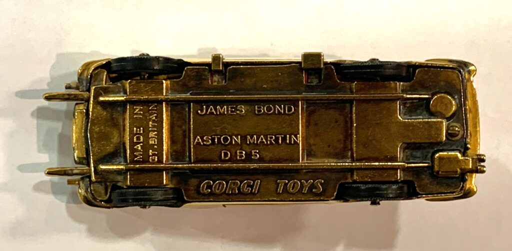 Image shows a close up of the underside of a gold coloured Corgi model of a DB5. It reads 'James Bond / Aston Martin / DB5', 'Corgi Toys' and 'Made in Great Britain'