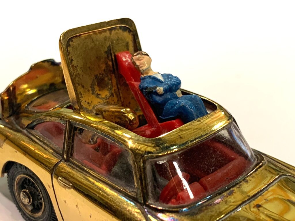 Image shows a close up of the baddy in a gold coloured Corgi model of a DB5, with the ejector seat raised