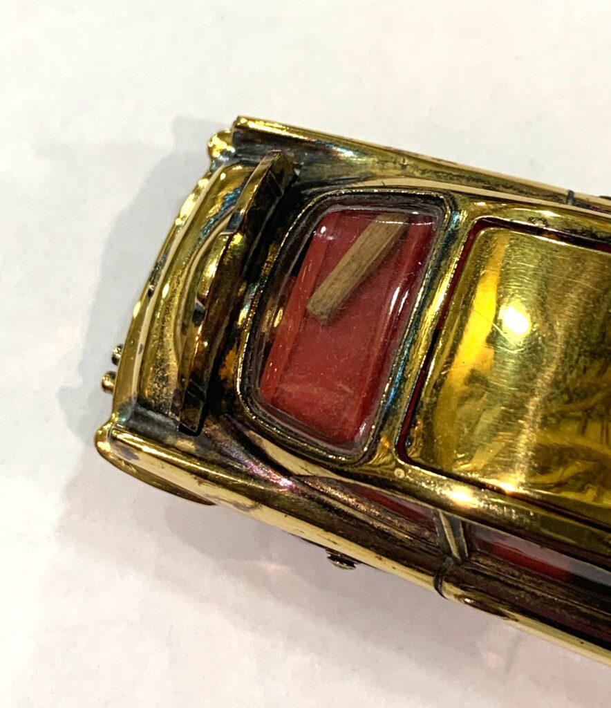 Image shows a close up of the small wooden club on the back seat of a gold coloured Corgi model of a DB5